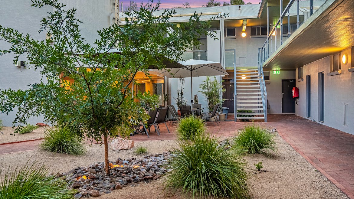 Outdoor courtyard with a tree, patio furniture under umbrellas, gravel landscaping, and a staircase leading to an upper floor.