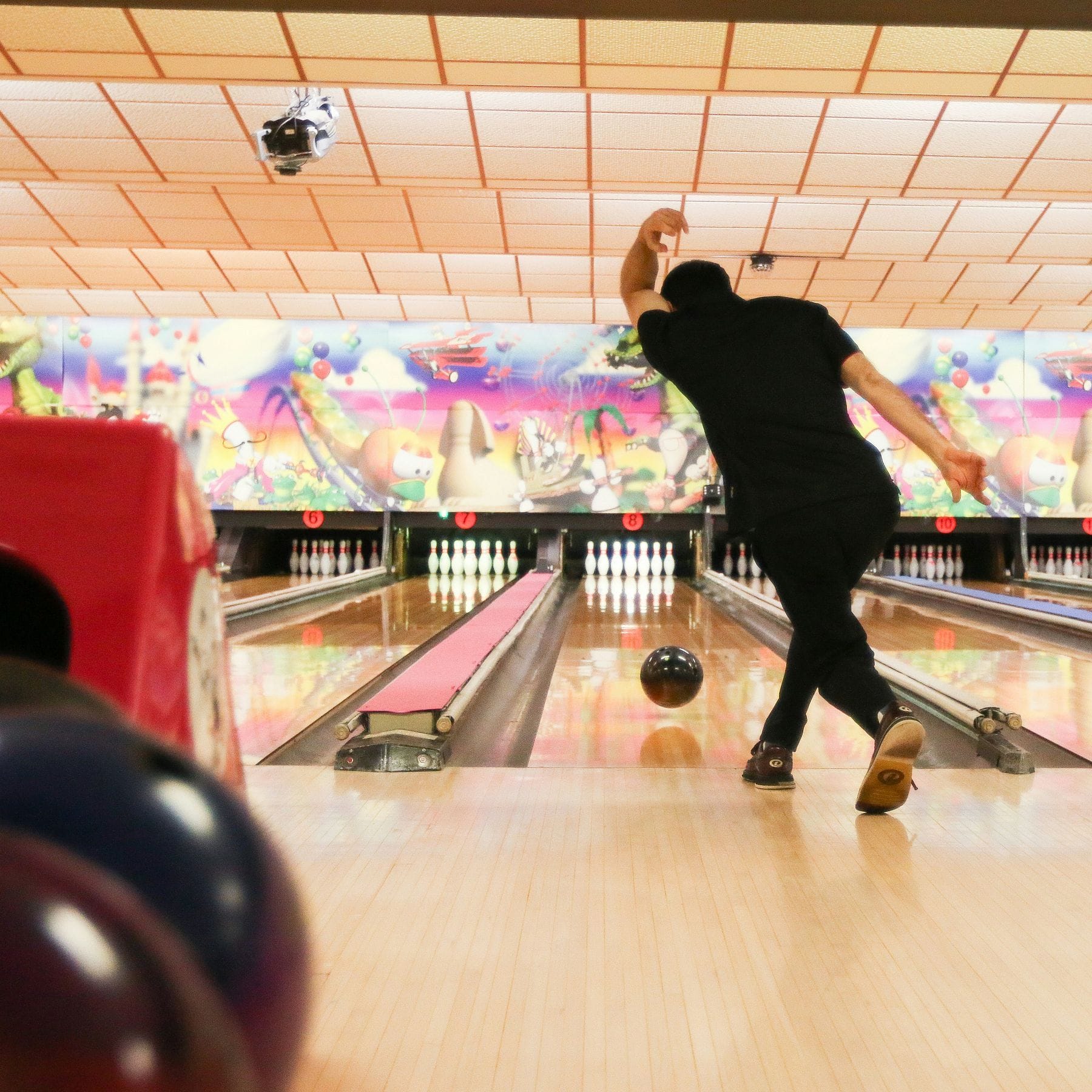 Person bowling in an alley, mid-throw, with colorful murals and pins visible in the background.