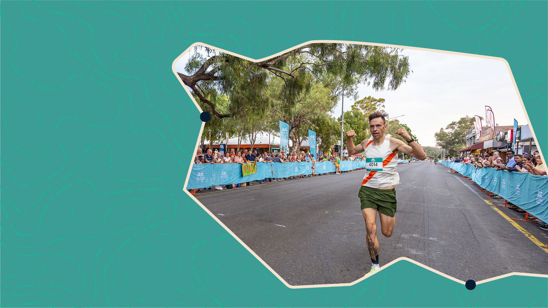 Runner in green shorts and white tank top nearing the finish line, surrounded by cheering crowds and blue banners on a city street.