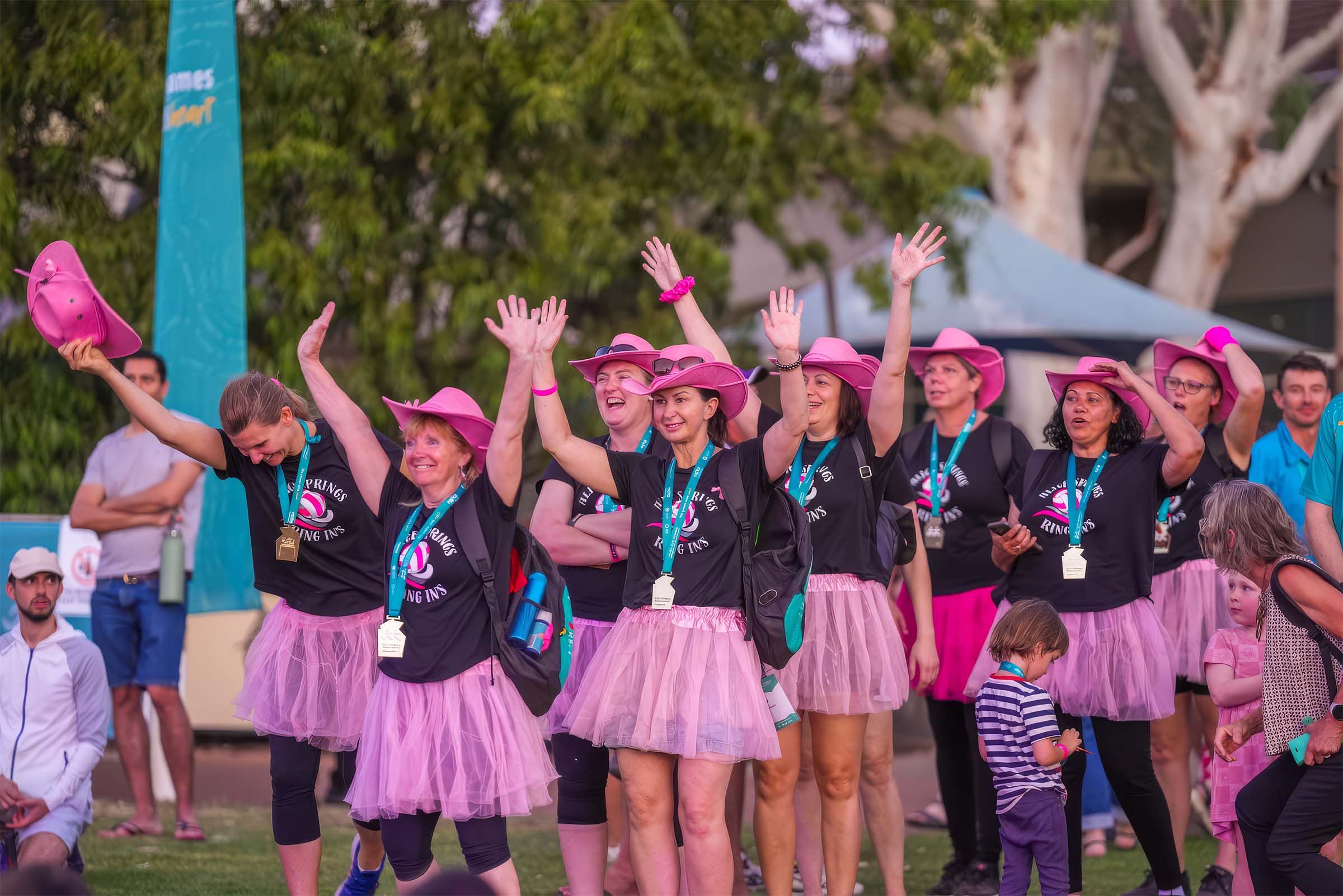 Group of women with arms raised wearing pink tutus and pink cowboy hats